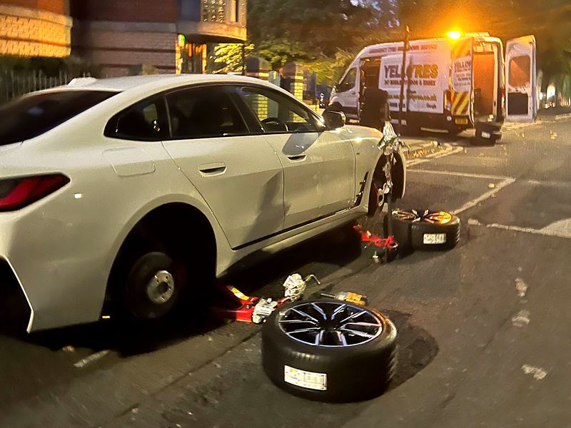 Mobile tyre fitter's van with beacon lit behind a BMW having a wheel changed at the roadside at dusk