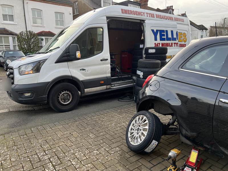 Black Fiat 500 on a trolley jack with a new tyre on its alloy, Yellow Tyres van parked on the street