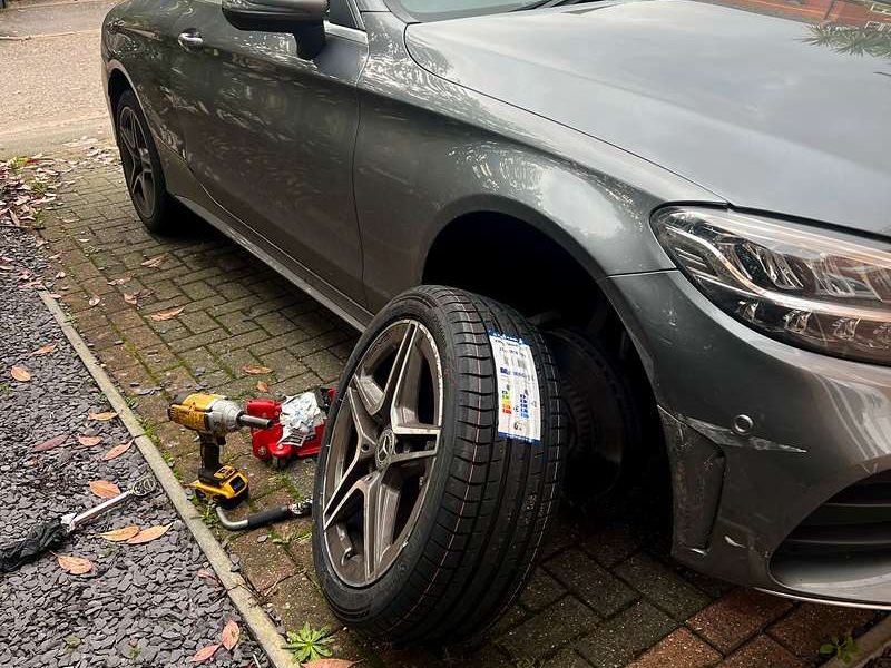 Grey Mercedes coupe on a block-paved driveway with a new labelled tyre ready to go on