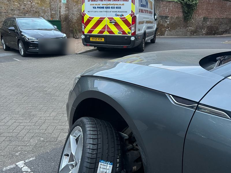 New tyre with its EU label fitted to a grey coupe in a residential car park, Yellow Tyres van with red and yellow chevrons behind