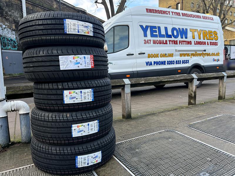 Five brand-new labelled tyres stacked beside the Yellow Tyres mobile fitting van