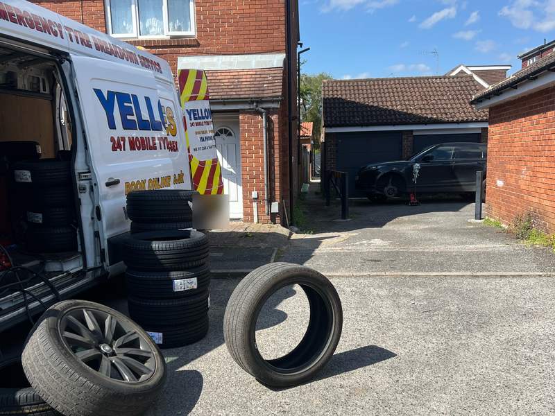 Worn tyres taken off and new tyres stacked beside the open Yellow Tyres van in a residential garage court