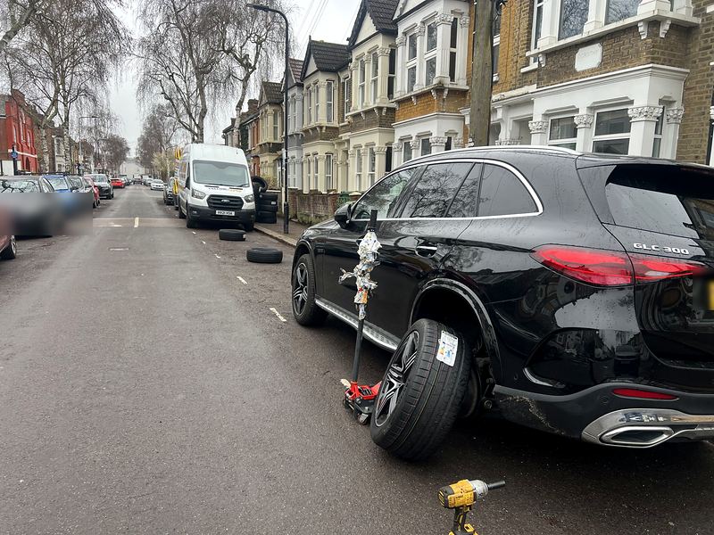 Mercedes SUV on a jack on a terraced street, Yellow Tyres van and tyres further up the road